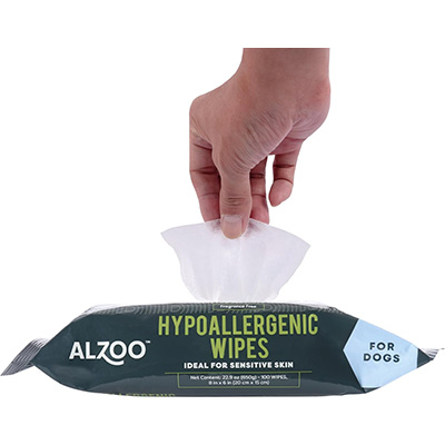 A hand pulls a wipe from a pack of ALZOO Hypoallergenic Wipes for dogs. The packaging is labeled “Ideal for Sensitive Skin” and emphasizes that the product is gentle and designed specifically for dogs.