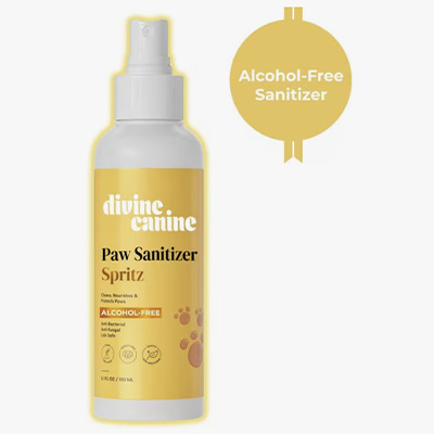 A yellow spray bottle labeled “Divine Canine Paw Sanitizer Spritz” with a white cap. The label notes that it's alcohol-free and safe for dogs, with paw print graphics and a round badge that also reads “Alcohol-Free Sanitizer.”